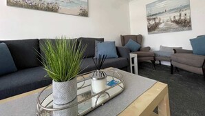 A living room with a sofa, a coffee table, a potted plant, and two paintings on the wall.
