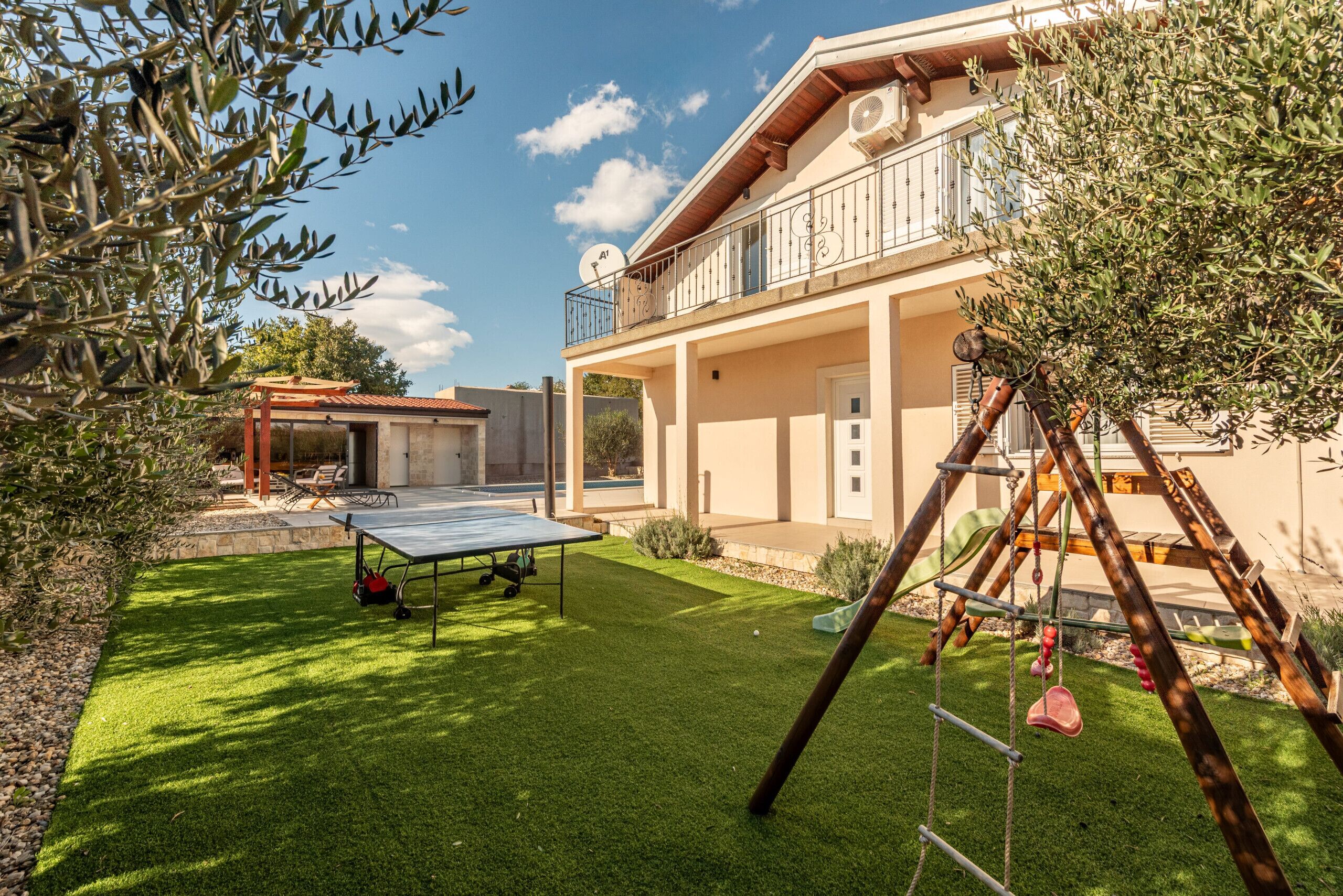 Una casa con balcón, mesa de ping pong y un columpio.
