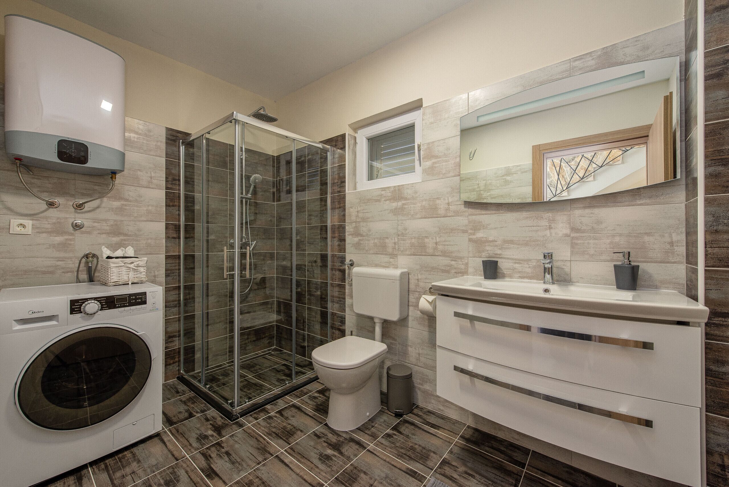 Une salle de bain moderne avec une douche à parois de verre, des toilettes, un lave-linge et un meuble-lavabo avec un miroir.