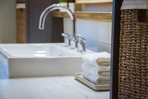 Ein modernes Badezimmer mit einem weißen Waschbecken, einem silbernen Wasserhahn und einer gewebten Fußmatte.