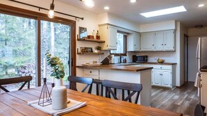Une cuisine moderne avec des meubles blancs, un plan de travail en bois et un coin repas comprenant une table et des chaises en bois.