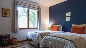 Une chambre avec deux lits, une fenêtre, une lampe et un tableau encadré au mur.