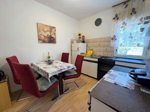 Eine kleine Küche mit Esstisch, Stühlen, Kühlschrank, Herd und einem Fenster mit Blick.