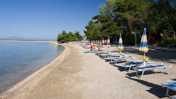 Een strand met ligbedden en parasols, heldere lucht en een rustige zee.