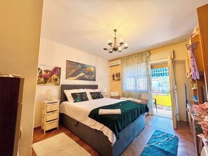 Ein Schlafzimmer mit Bett, Nachttischen, einer Chandelierleuchtre und einem Fenster mit Vorhängen und Blick ins Freie.