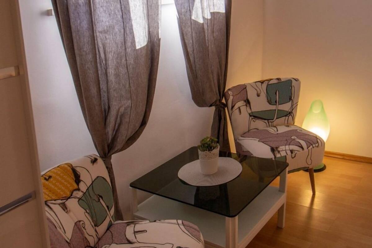 Une petite pièce agréable, avec une table et deux chaises, une plante en pot et une lampe verte.