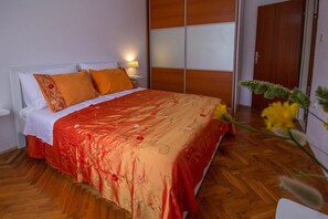 Une chambre d’hôtel avec un plancher en bois, un lit recouvert d’une courtepointe à motifs floraux rouge et orange, des oreillers blancs et une table de chevet avec une lampe.