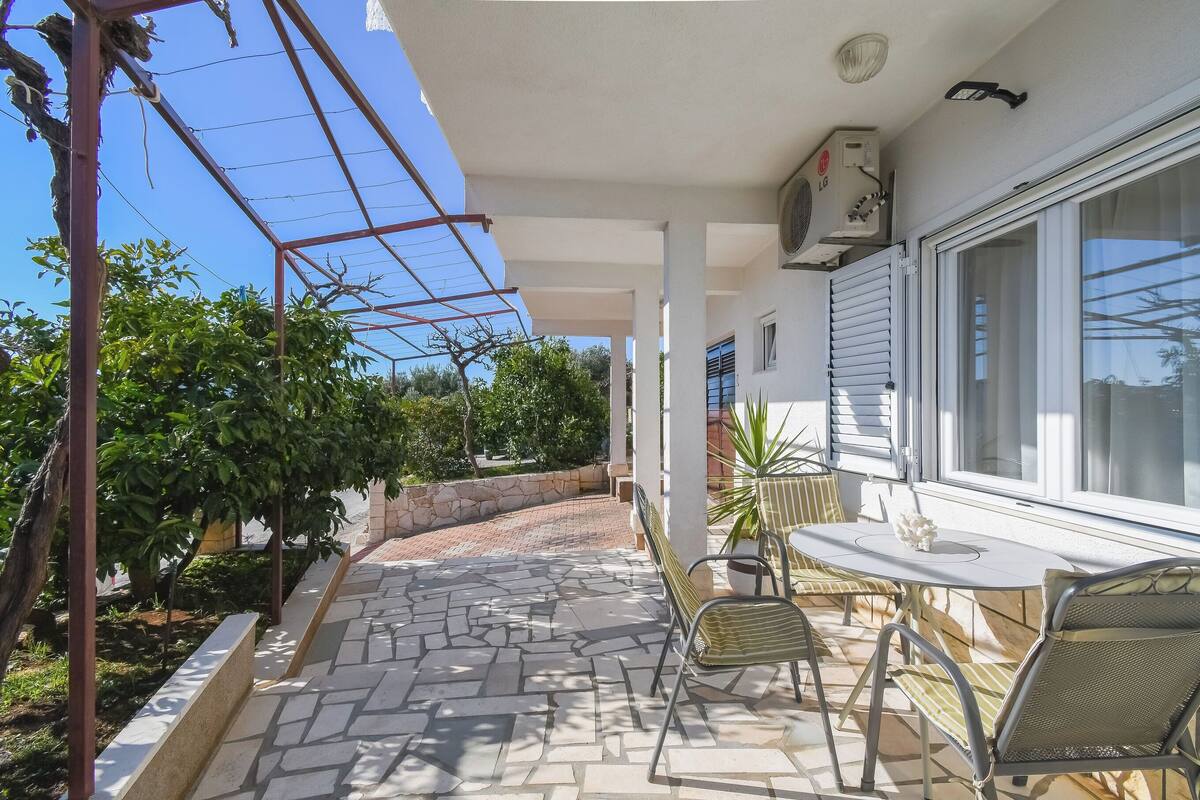 Un patio cubierto con piso de piedra, sillas de metal, una mesa y una planta en maceta.