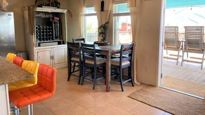 Uma sala de jantar com mesa e cadeiras, geladeira, espaço para vinhos e vista para o exterior.