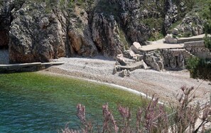 A rocky shoreline with a clear blue pool, stone steps leading down to the water, and a rocky cliff in the background. - Luka - With Parking - A2 (Vrbnik)
