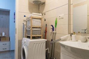 A bathroom with a washing machine, a shelf with folded towels, a sink, and a mirror. - Snjezanal- in the Center - A1 (Split)