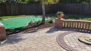 A patio area with a brick floor, a circular wooden table, and a green artificial turf. - Minutes to gulf beaches, great outdoor space, putting green,perfect getaway  (Englewood)