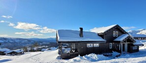 Eine Holzhütte mit schneebedecktem Dach, der deutlich sichtbaren Nummer '77' und einer malerischen Bergkulisse.