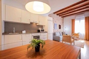 Une cuisine moderne avec des meubles blancs, un îlot central agrémenté d’une plante et un coin repas avec une table en bois.