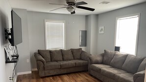Ein Wohnzimmer mit zwei Sofas, einem Deckenventilator und einem flachbildfernseher an der Wand.