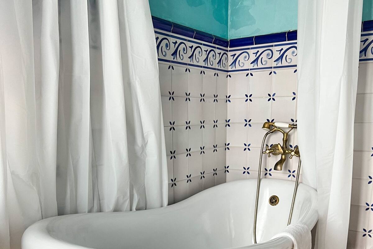 A bathroom with a freestanding bathtub, white tiles with blue patterns, and a tiled floor.