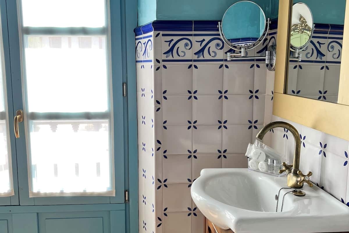 A bathroom with a white sink, blue and white patterned tiles, a mirror, and a window with a view of buildings.