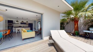 Un espacio habitable moderno con cocina, comedor y un patio con sillón blanco y una palmera.