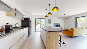Una cocina moderna con una isla central, iluminación colgante y un comedor con sofá y mesa.