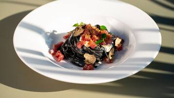 Un plato blanco con una porción de pasta negra adornada con tomates rojos y hojas verdes.