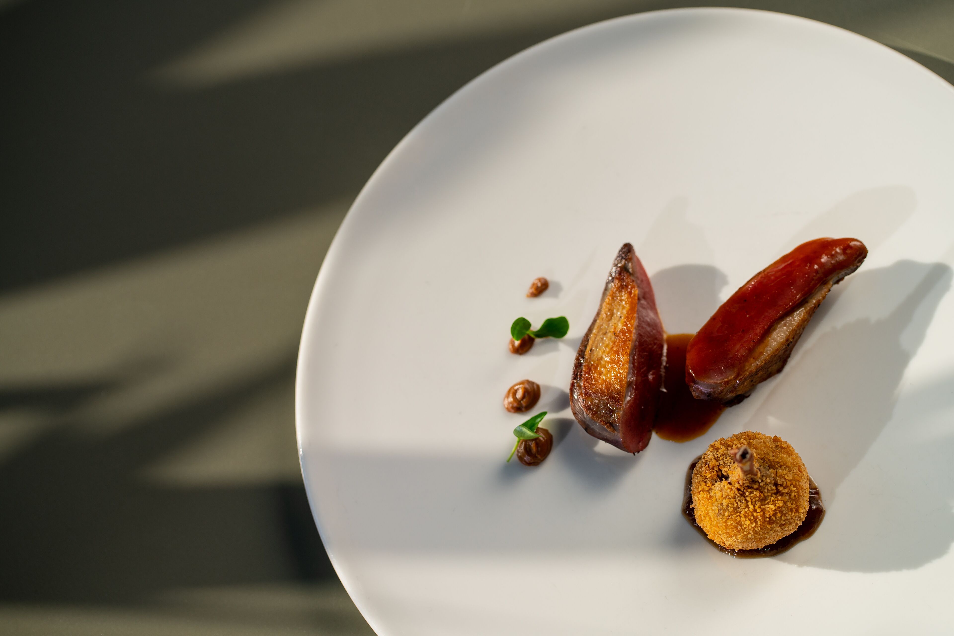 Une assiette blanche contenant un plat composé d’un morceau de viande, d’un élément rond et de quelques petites garnitures.