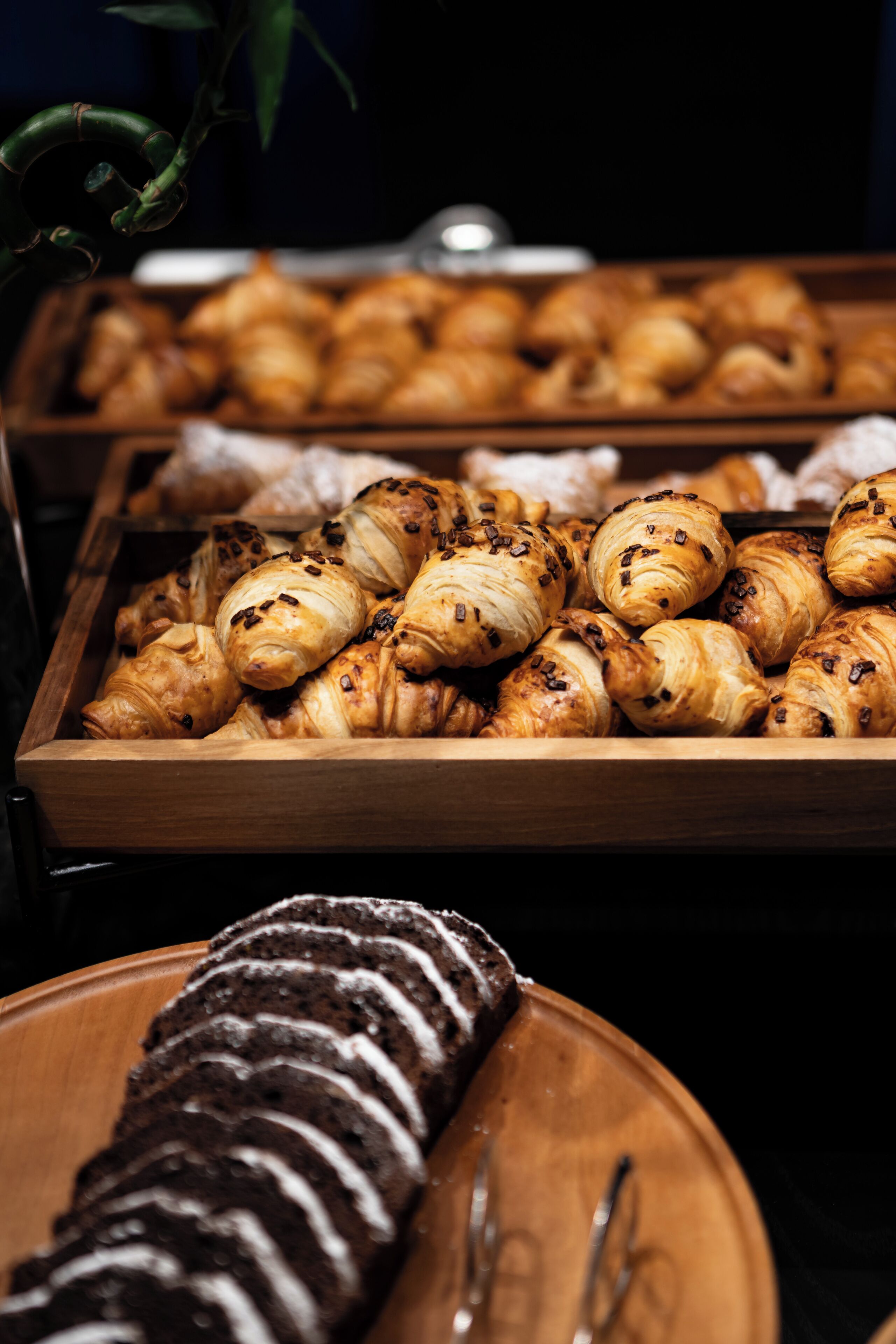 A variety of pastries displayed in wooden trays, including croissants and chocolate-covered items.