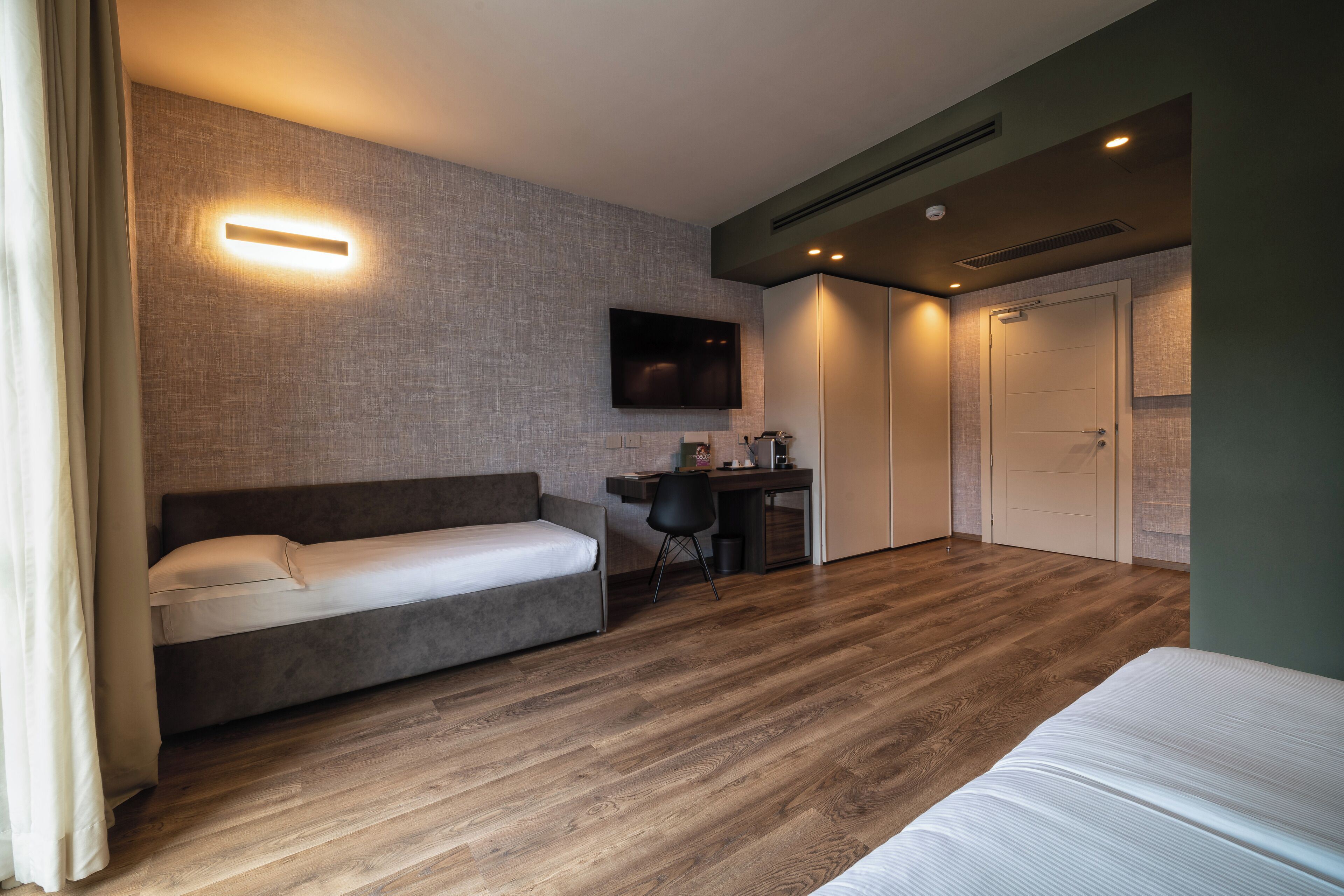 A modern hotel room with a sofa, a desk, a TV, and a wardrobe.