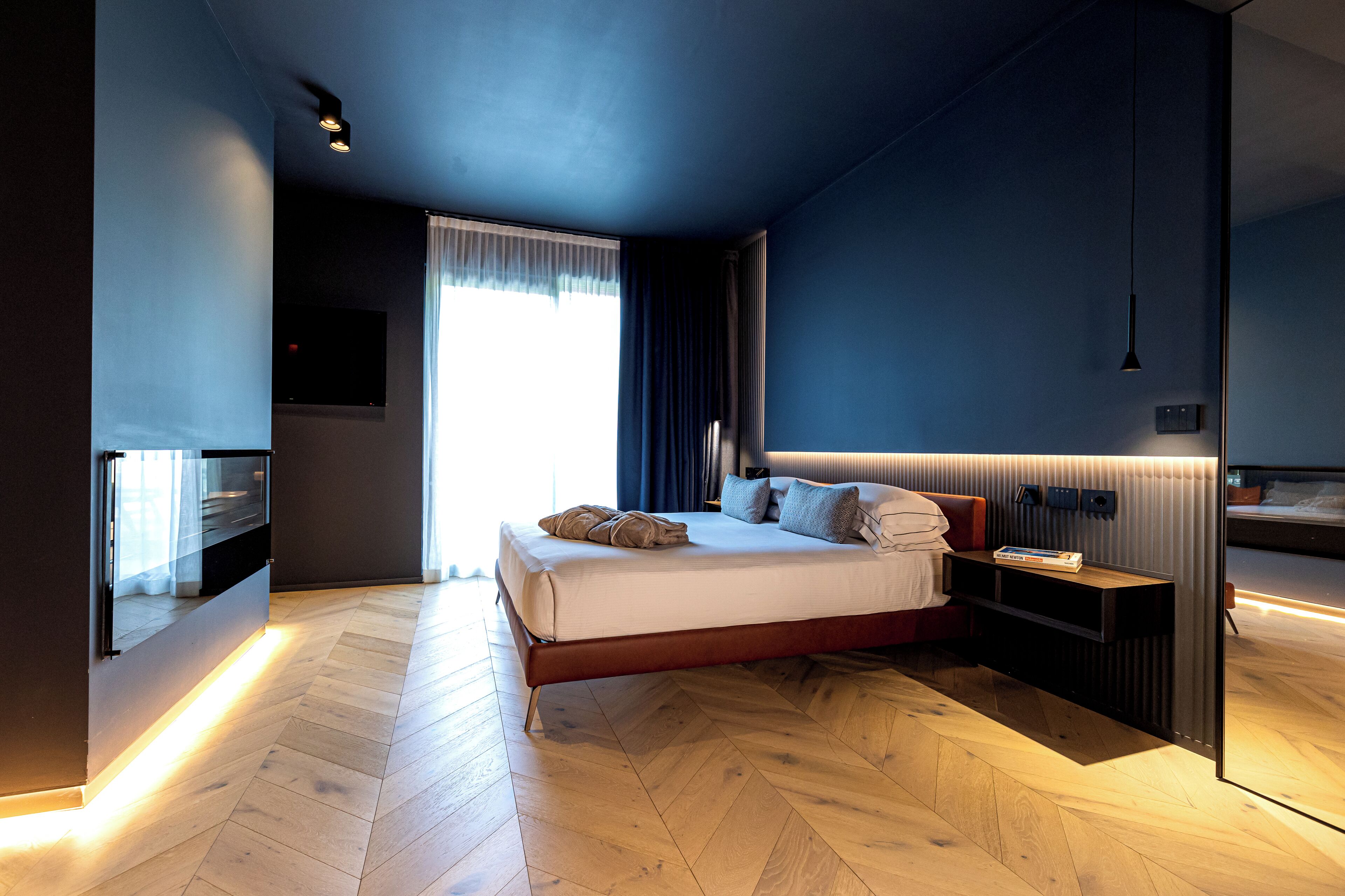 Un dormitorio moderno con una cama grande, una mesita de noche, un televisor y una ventana con cortinas.