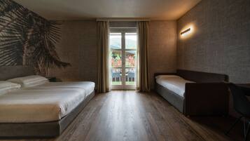 A modern hotel room with two beds, a wooden floor, a large window with curtains, and a wall-mounted light fixture.