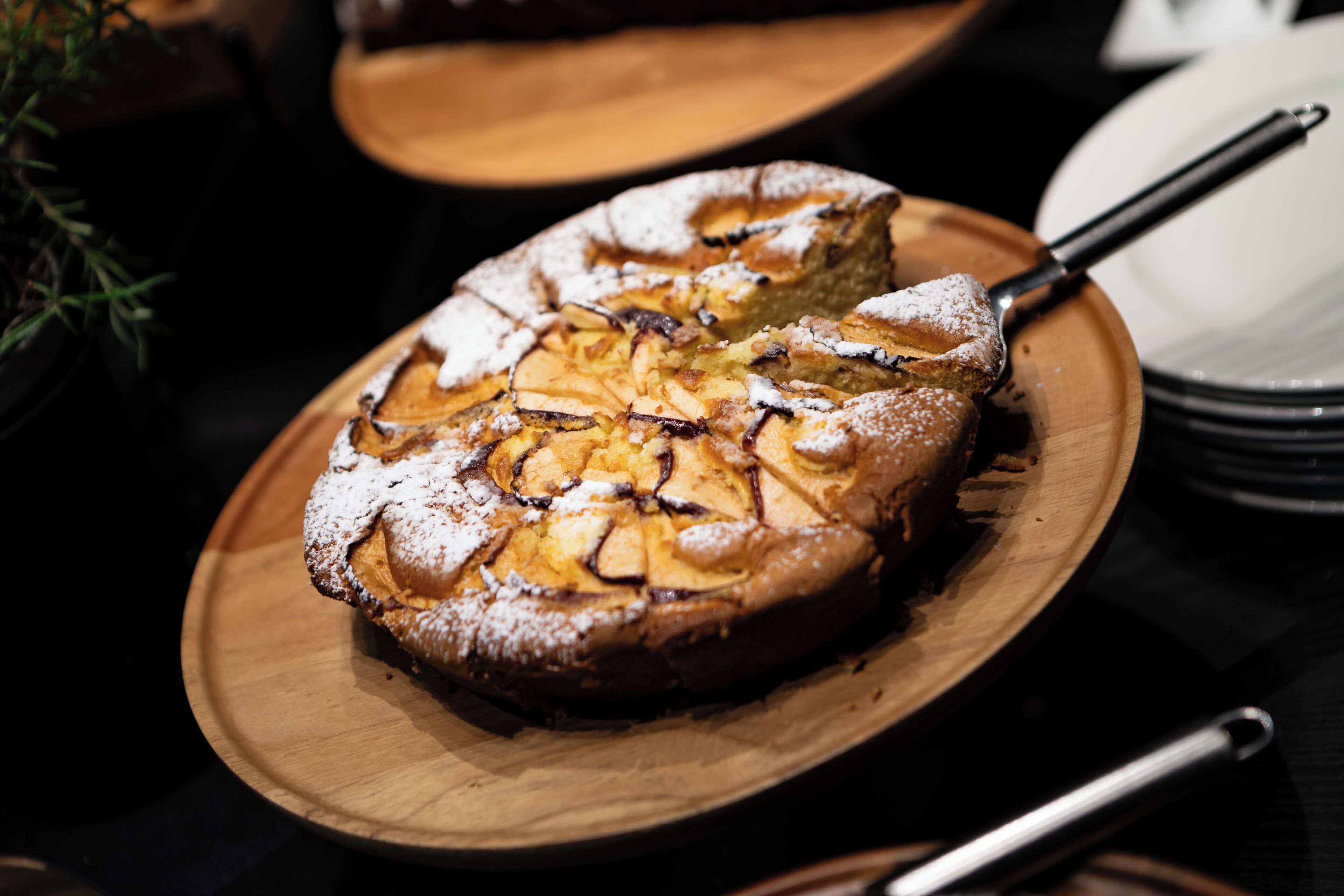 Un gâteau rond, garni de fruits coupés en tranches et saupoudré de sucre glace, présenté sur une assiette en bois.