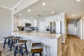 A spacious kitchen with white cabinetry, a large island with stools, stainless steel appliances, and a wooden floor.