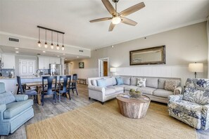 A spacious living room with a large ceiling fan, a dining area with wooden chairs, and a kitchen in the background.