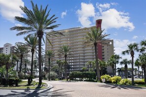 A multi-story hotel with a central tower, surrounded by palm trees and a paved walkway.