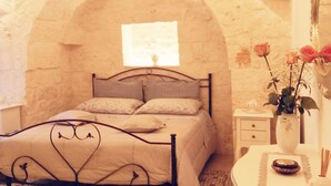 Un dormitorio con cama, mesita de noche, cómoda, espejo y un jarrón con flores.