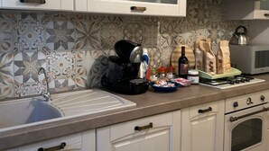 Una cocina con armarios blancos, microondas, hervidor y estufa a gas.