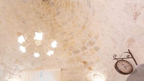 Una habitación con techo de piedra, una araña, un reloj de pared y una ventana con cortinas traslúcidas.