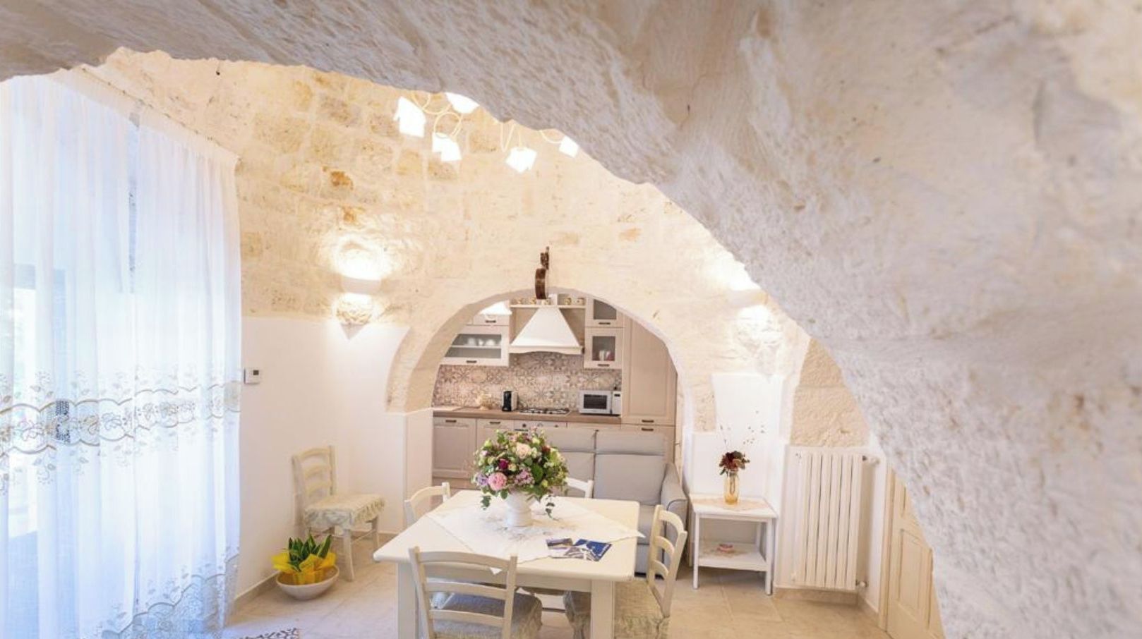 Une cuisine chaleureuse et rustique, avec des murs en pierre, un îlot central et un coin repas comprenant une table et des chaises.