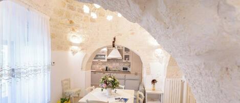 Une cuisine chaleureuse et rustique, avec des murs en pierre, un îlot central et un coin repas comprenant une table et des chaises.