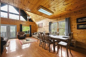A wooden cabin interior with a dining area, sofa, and large windows. - Free Attractions, Hot Tub, Pool Table, Resort Pool, Easy Access, Fishing Pond (Sevierville)