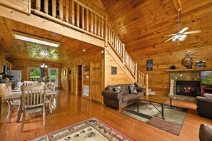 A cabin interior with a wooden staircase, a fireplace, a dining area with a table and chairs, and a living room with a sofa and a coffee table. - Free Attractions, Hot Tub, Pool Table, Resort Pool, Easy Access, Fishing Pond (Sevierville)