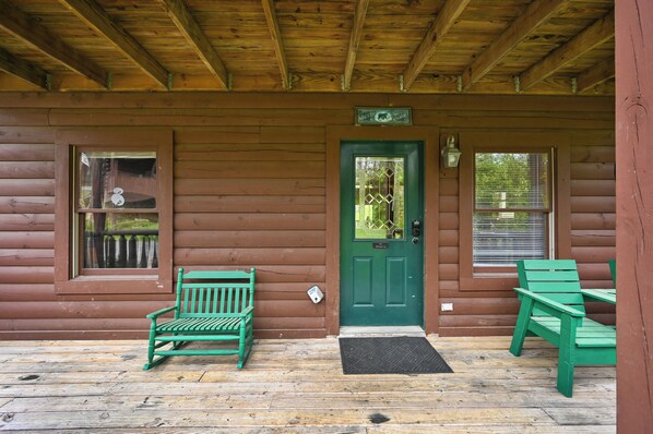 Une cabane en bois avec une porte verte, deux fenêtres et un porche doté de bancs verts.