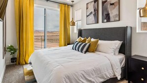 Een slaapkamer met een bed, een plafondventilator, een raam met gele gordijnen en uitzicht op de woestijn.