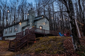 A house with a staircase leading to a deck, surrounded by trees.
