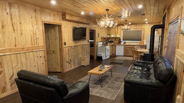 Ein Holzblockhaus-Innenraum mit einem Wohnbereich, der zwei schwarze Ledersofas, einen Holzesstisch und eine Küche mit Herd und Mikrowelle zeigt.