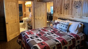 Ein gemütliches Zimmer mit Holzbalkendecke, einem Bett mit kariertem Überwurf, einem Nachttisch und einem Spiegel.