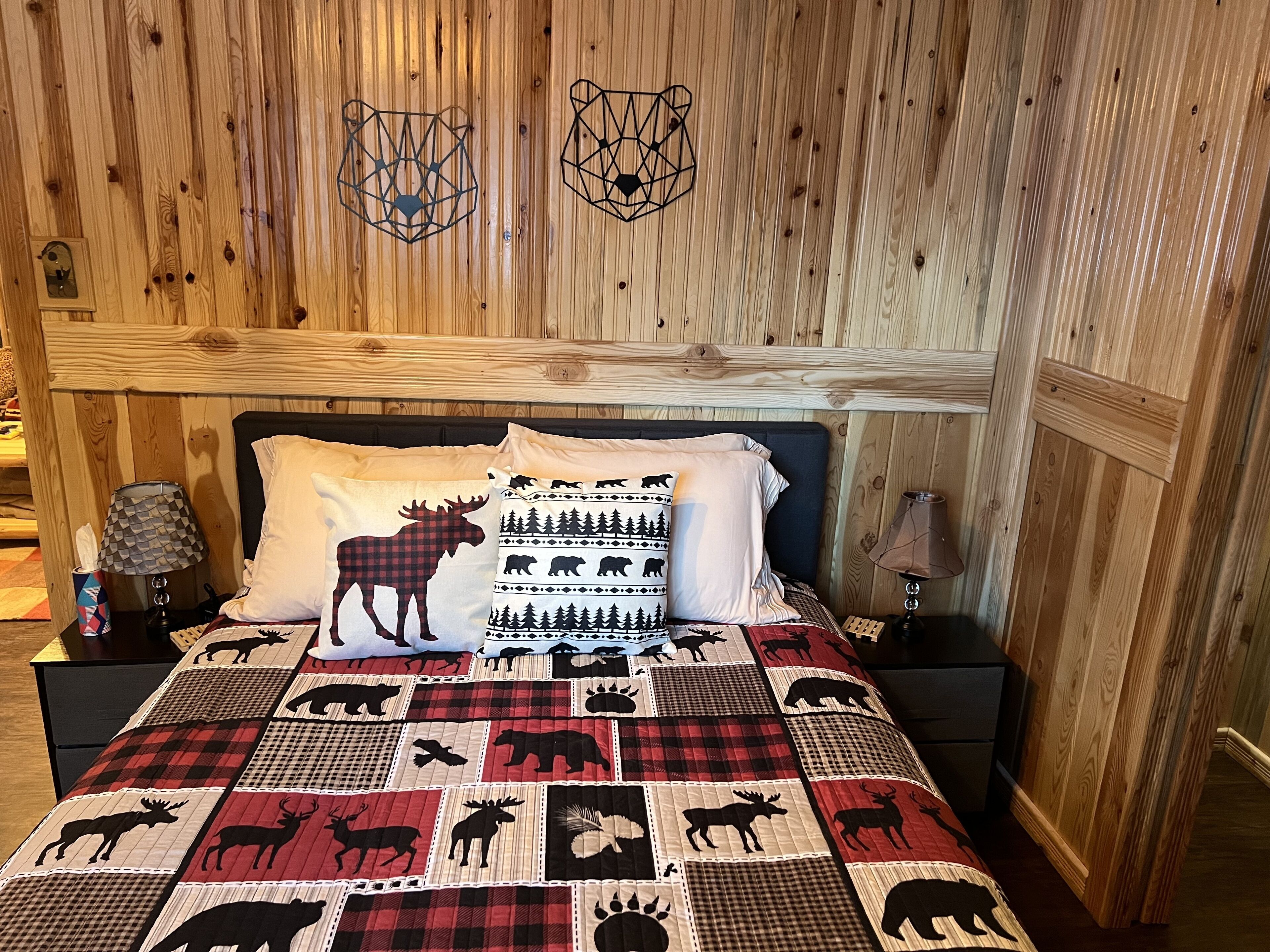 A wooden-paneled room with a bed featuring a quilted animal print bedspread and two wall-mounted geometric decorations.
