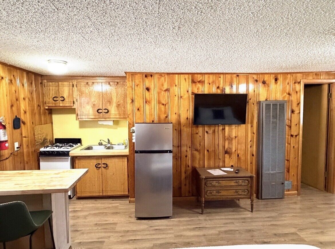 Una cocina con armarios de madera, un refrigerador, una estufa y un televisor.