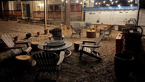 Eine Terrassenanlage im Freien mit Adirondack-Stühlen, einem runden Tisch und einem Grill.