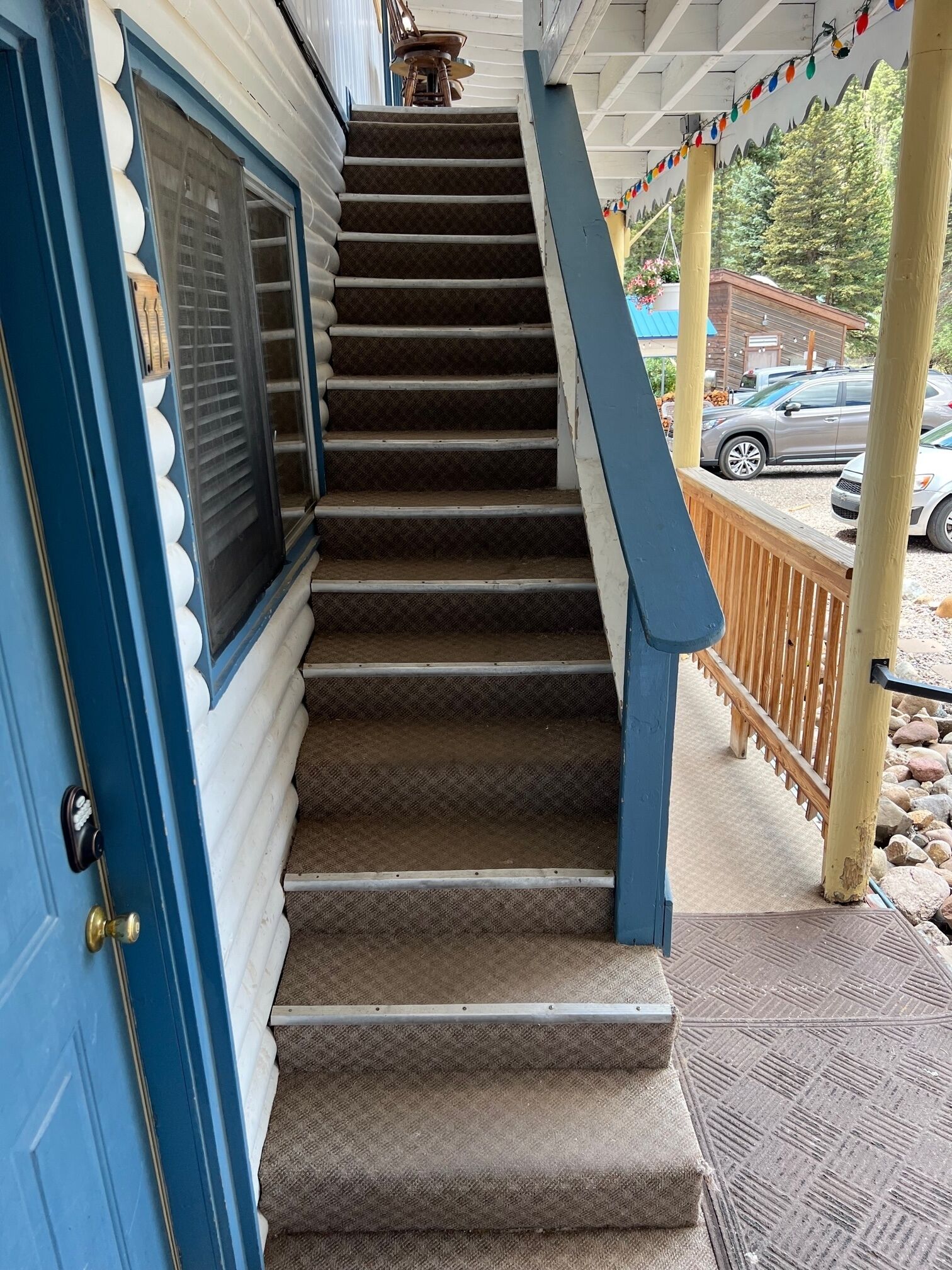 A staircase leading to a covered porch with a railing, a blue door, and a window with blinds.