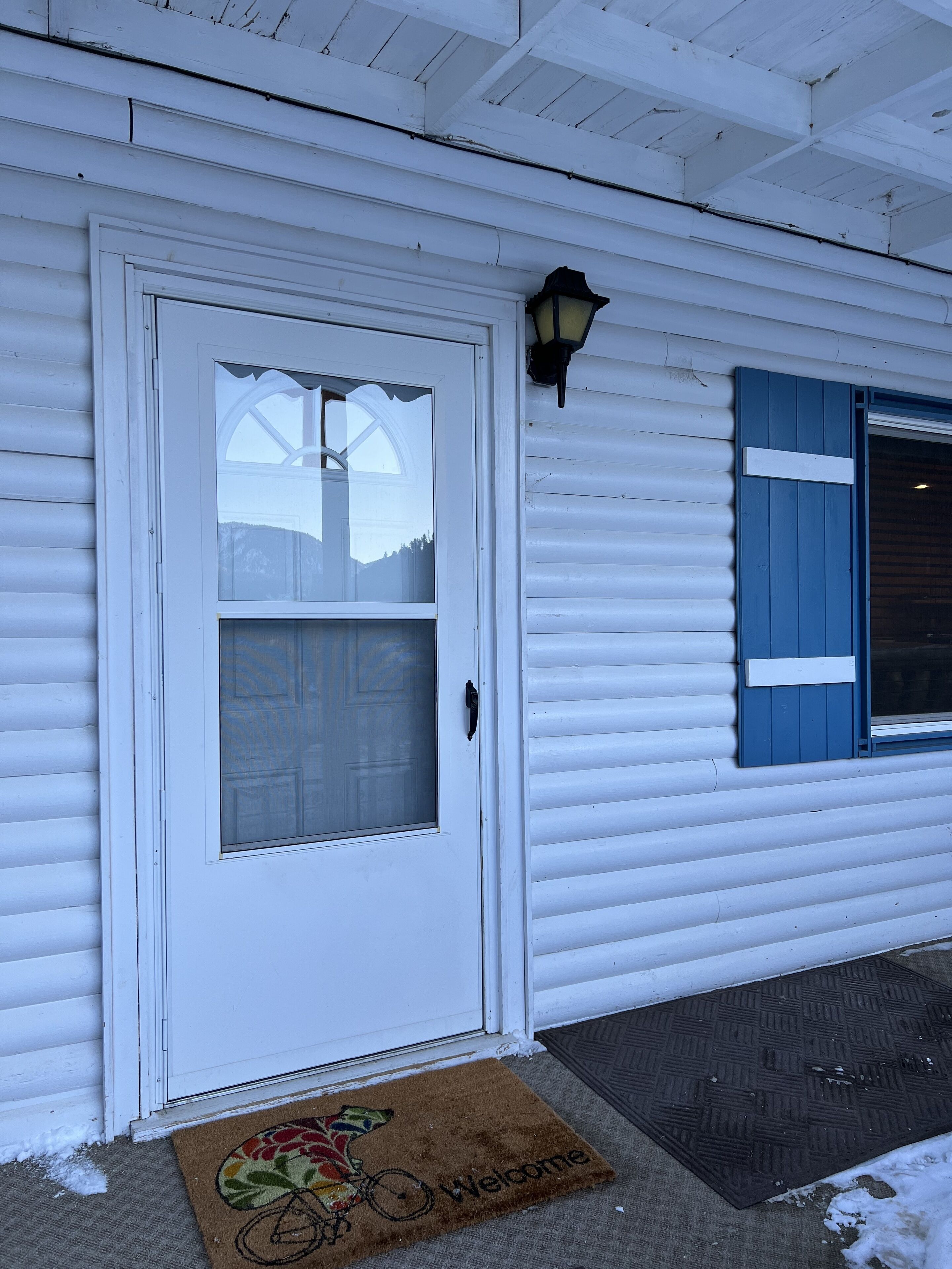 A white house with a white door, a window with blue shutters, and a welcome mat.